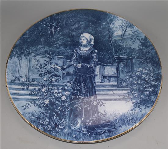 A blue-glazed circular ceramic wall plaque depicting a medieval lady in a garden, Dia 16in approx